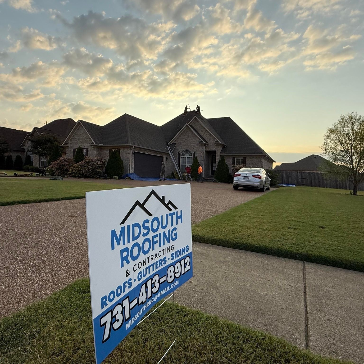 MidSouth Roofing yard sign in front of a suburban house at sunset, with a worker near the entrance.