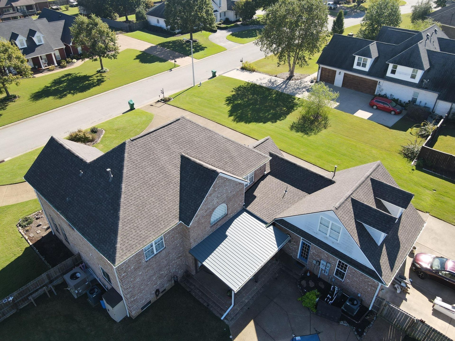 Aerial view of a suburban house with gray roof and brick walls on a tree-lined street.