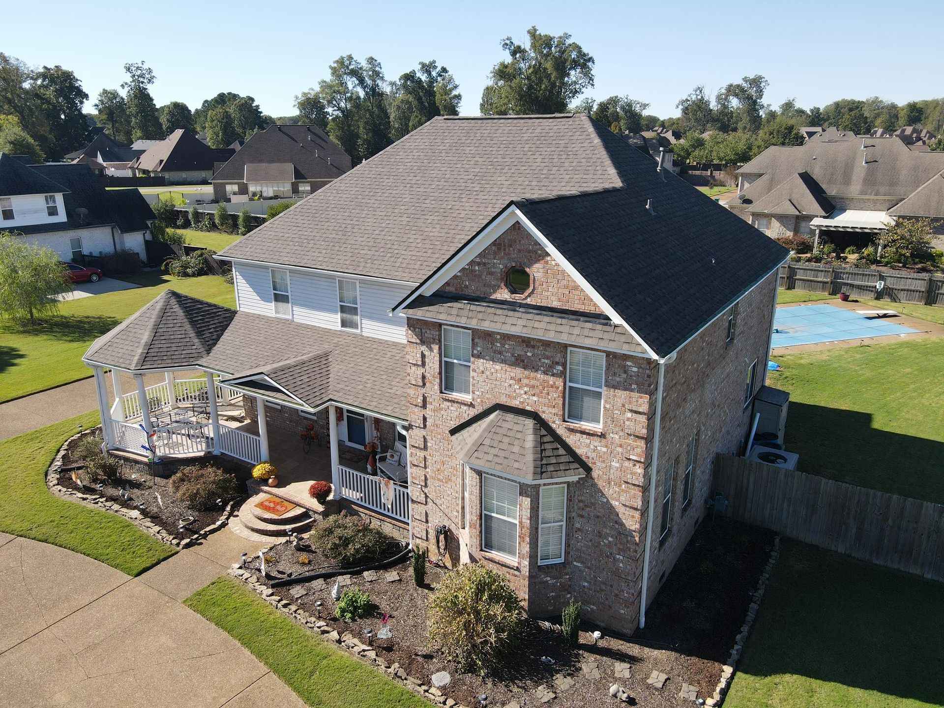 Aerial view of a two-story brick house with a screened porch, driveway, and landscaped yard near a cul-de-sac
