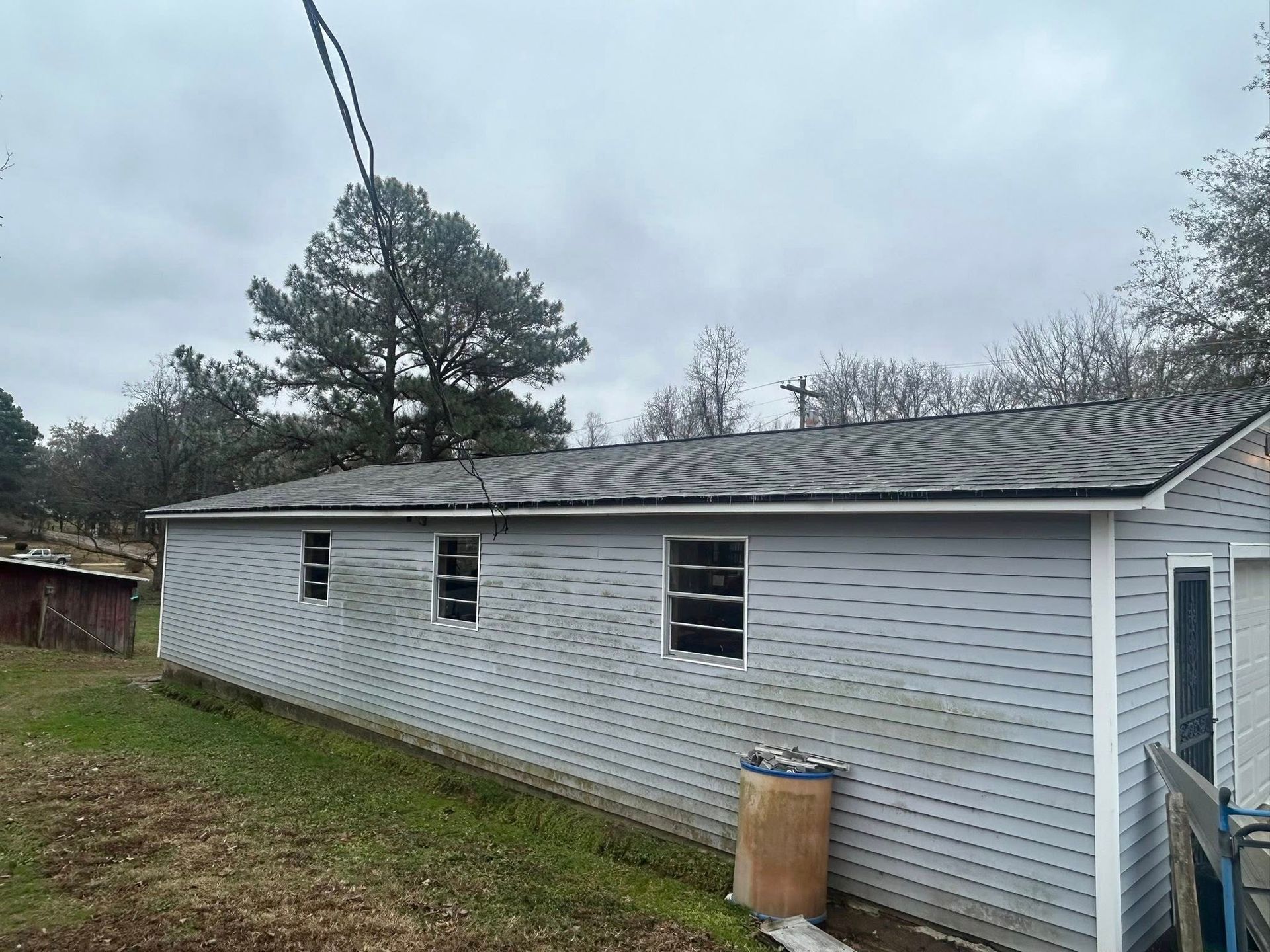 Gray single-story house with a sloped roof, small windows, and a grassy yard on a cloudy day