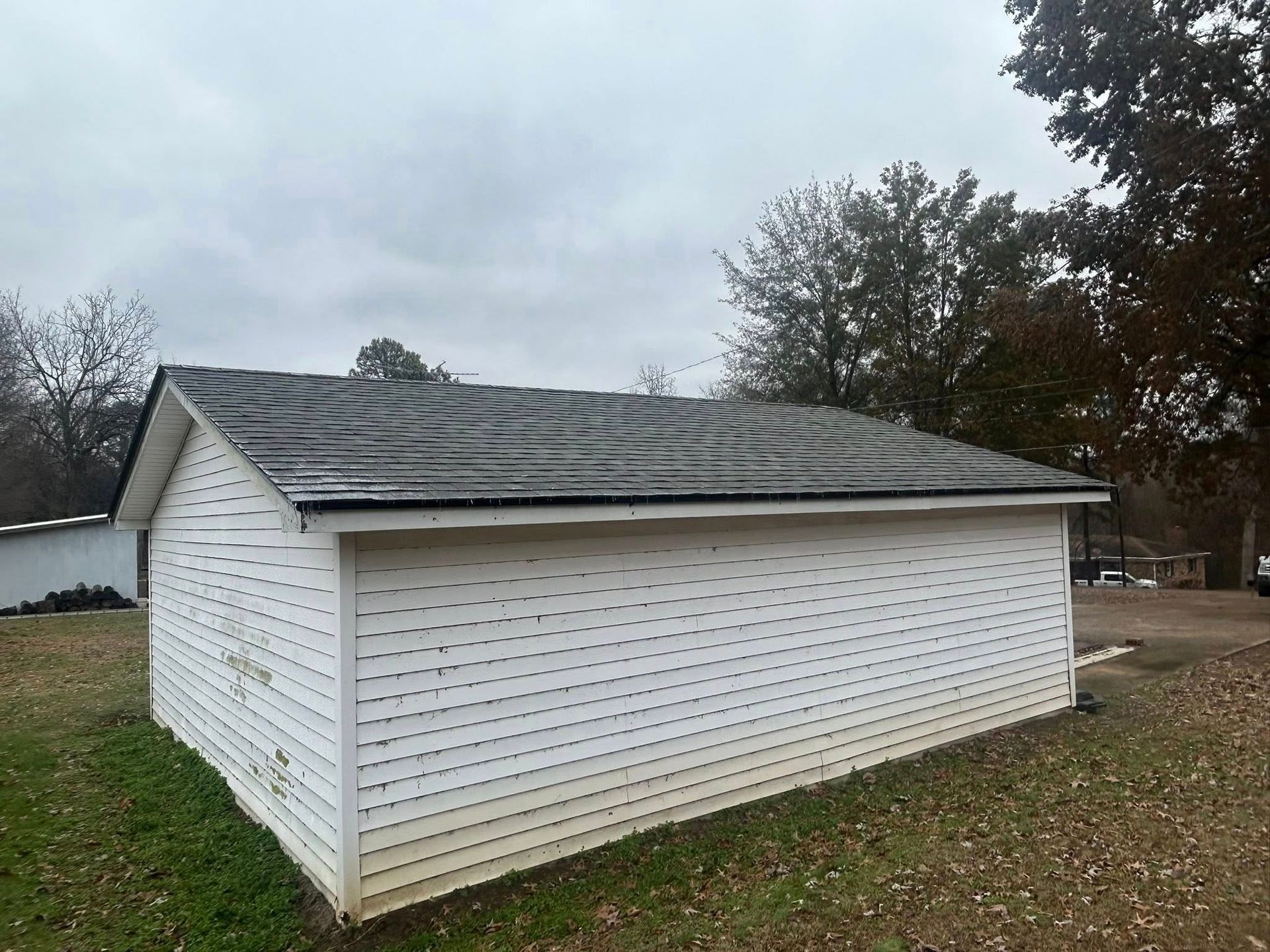 White detached garage with a weathered shingle roof in a grassy yard under cloudy skies