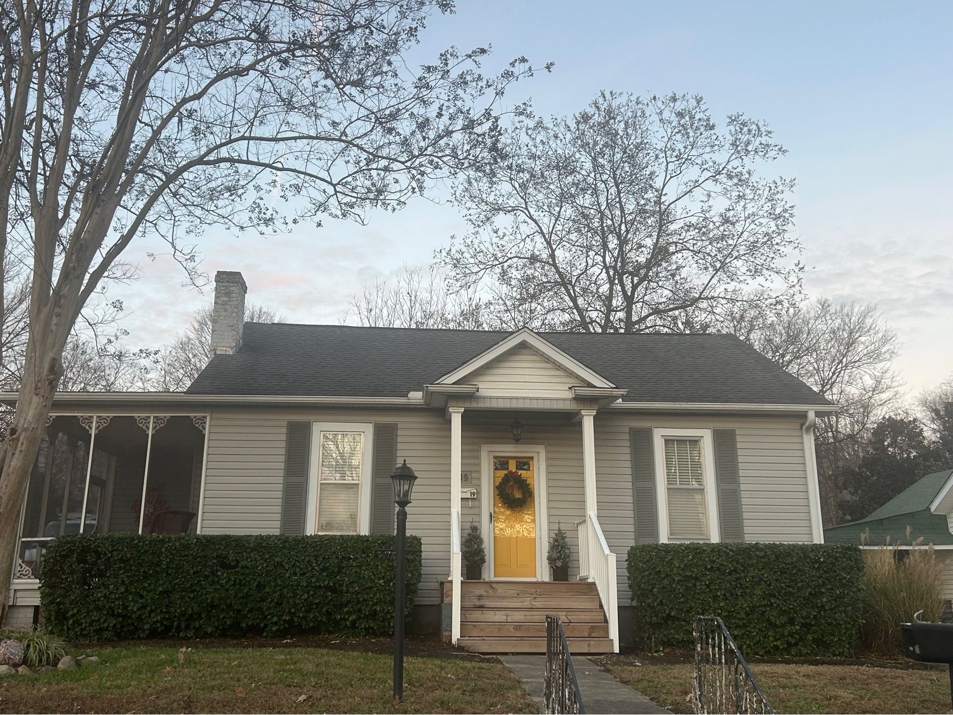 Small gray house with white trim, front porch, yellow door, and bare trees in a quiet neighborhood.