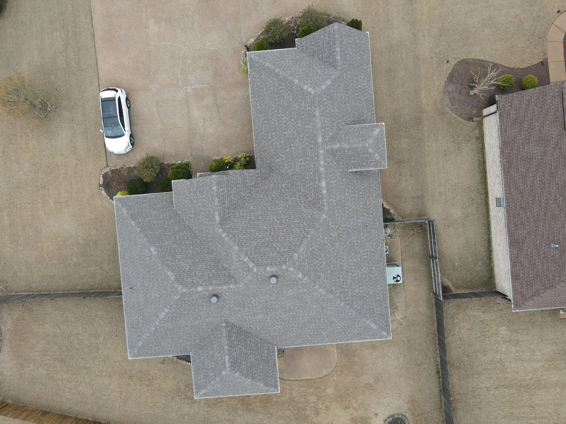 Aerial view of a house with a gray roof, driveway, parked white car, and neighboring homes.