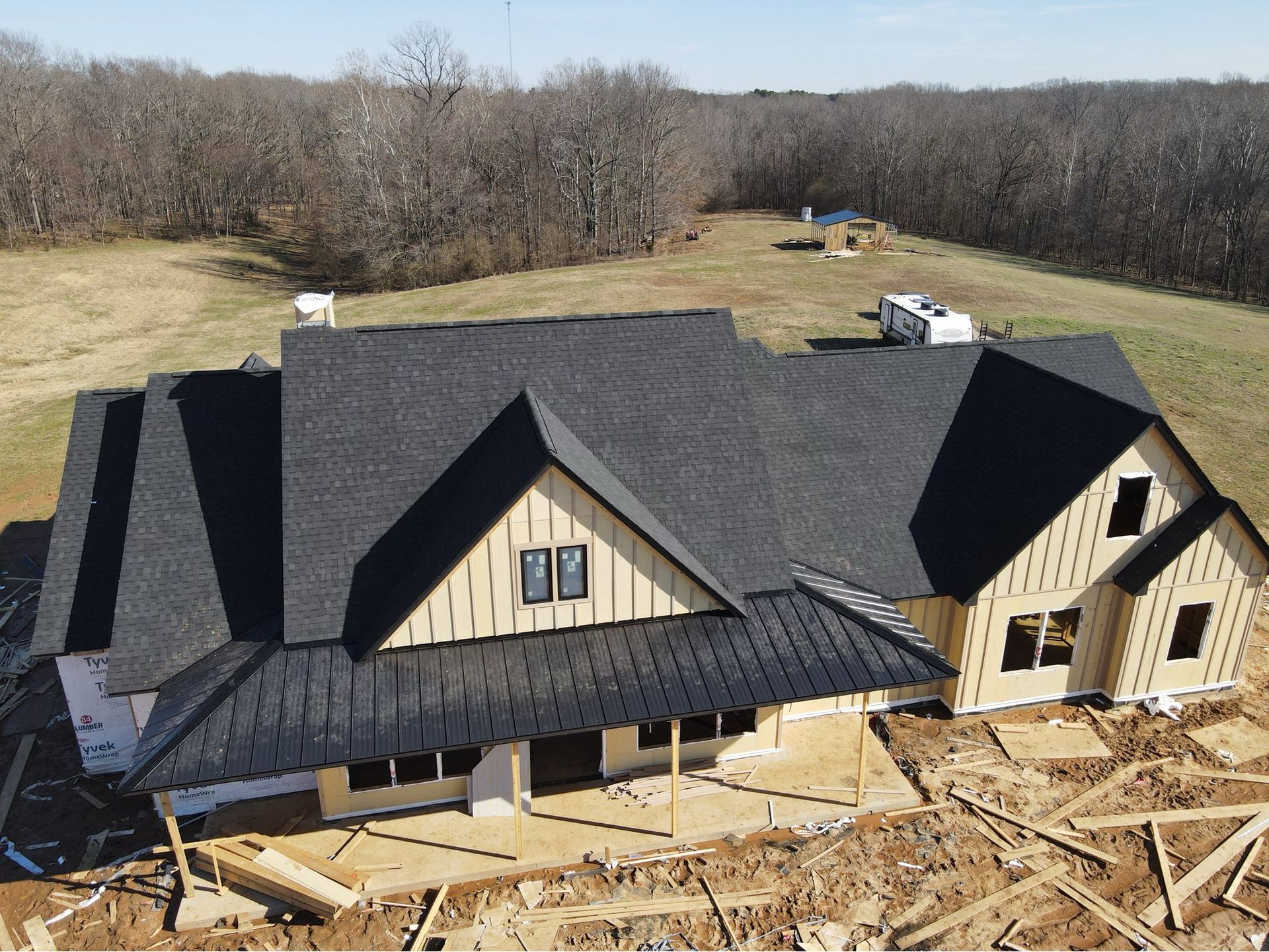 New house under construction with dark roof, tan siding, and lumber scattered in front