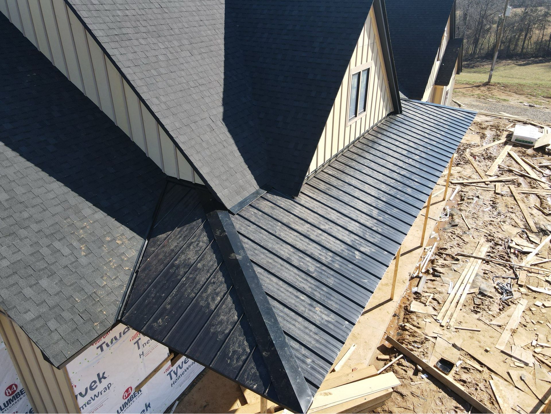 Roof with dark gray shingles and a long black metal ledge above a construction site