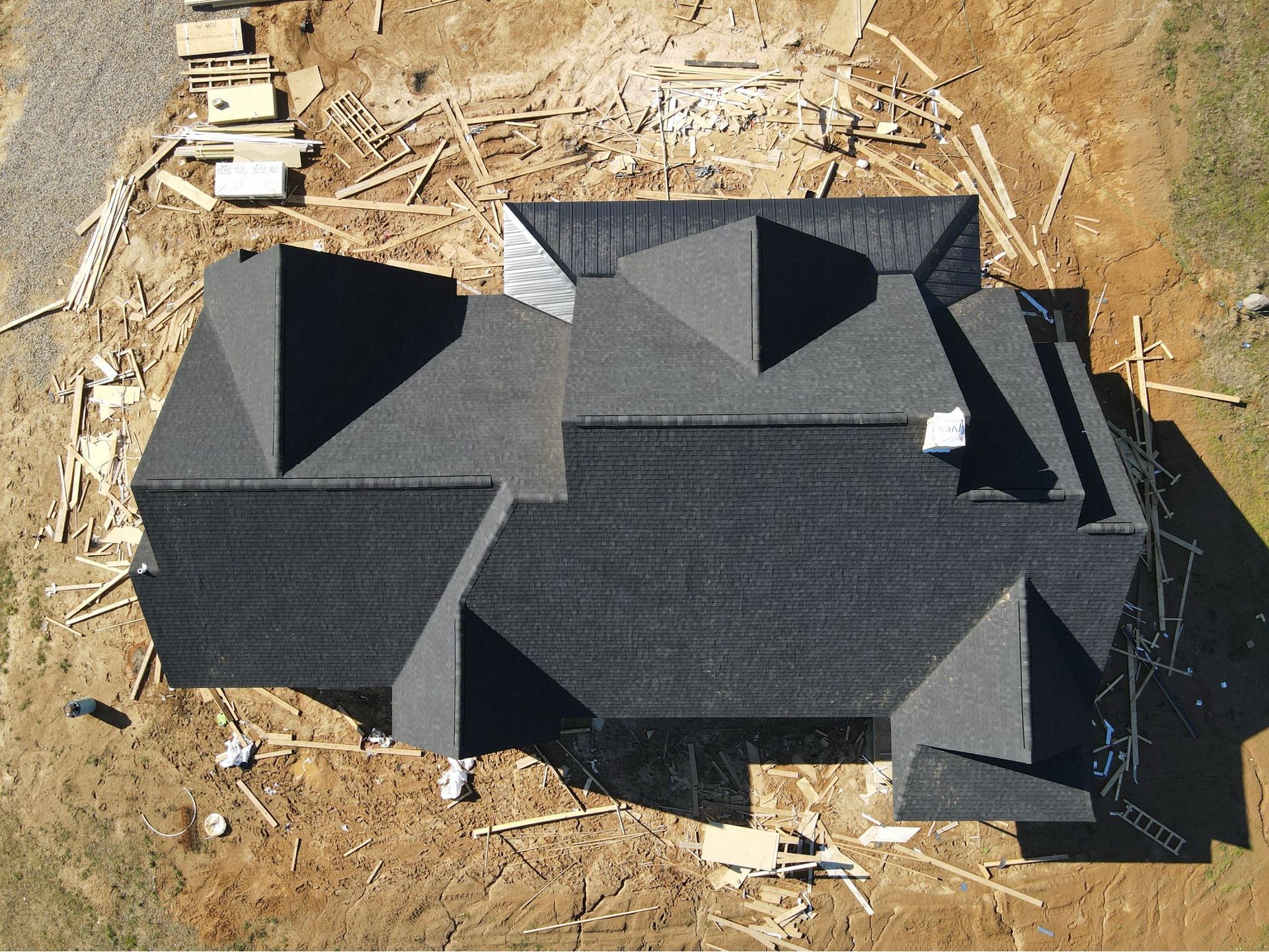 Aerial view of a large dark-roofed house under construction on a dirt lot.