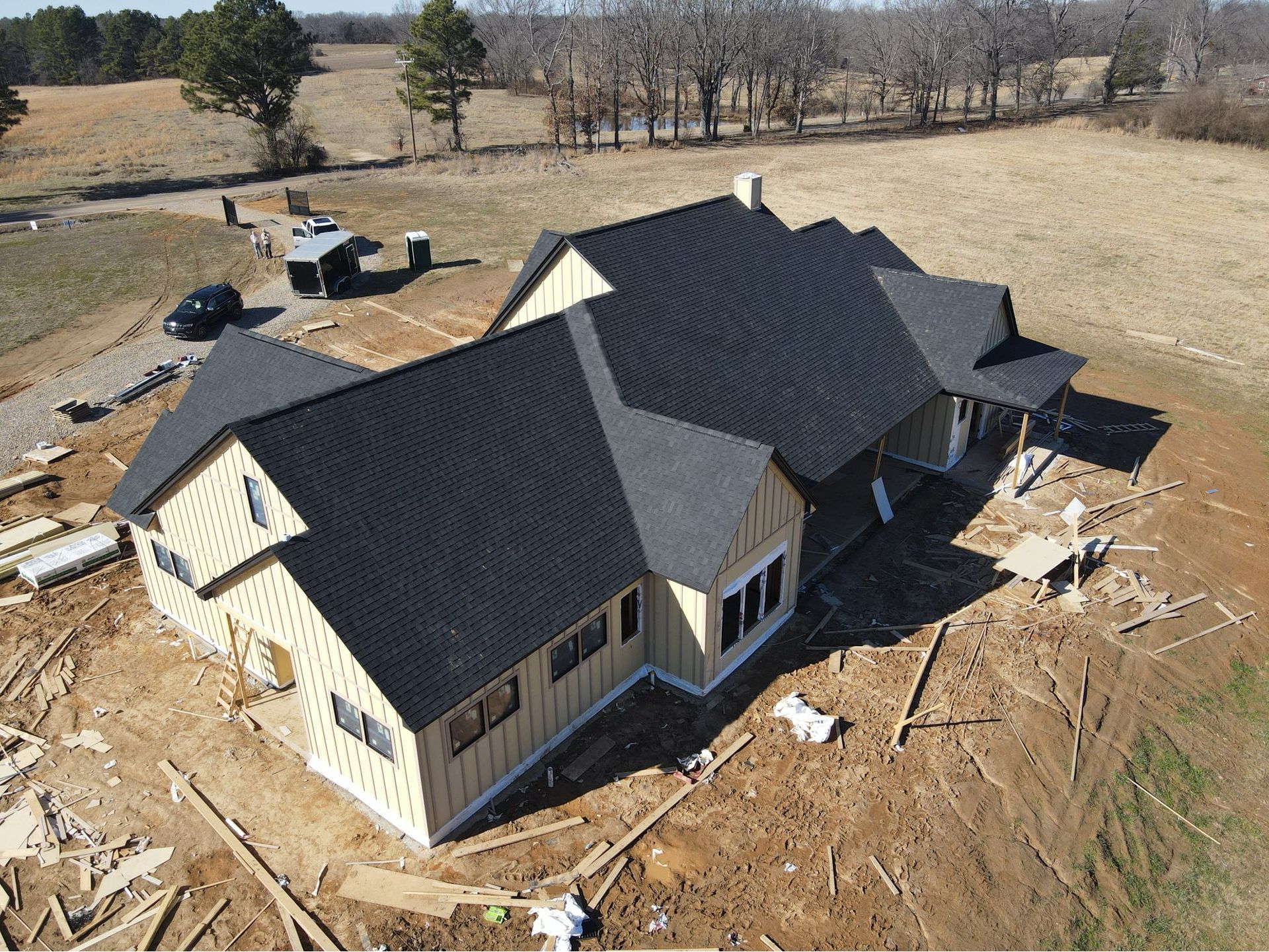 Aerial view of a new house under construction with a dark roof and bare dirt yard.