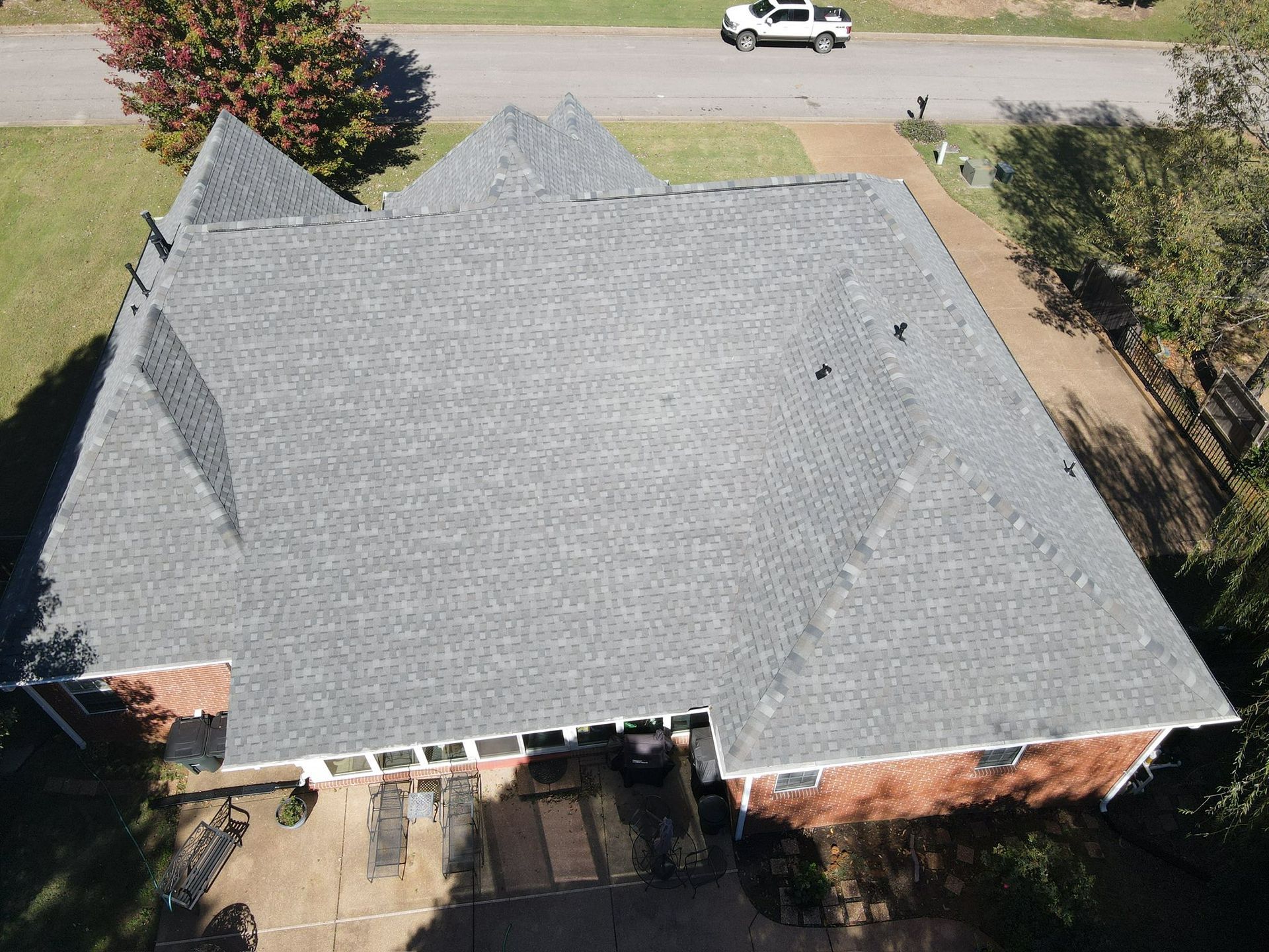 Aerial view of a gray-shingled house roof with brick walls and a driveway below.
