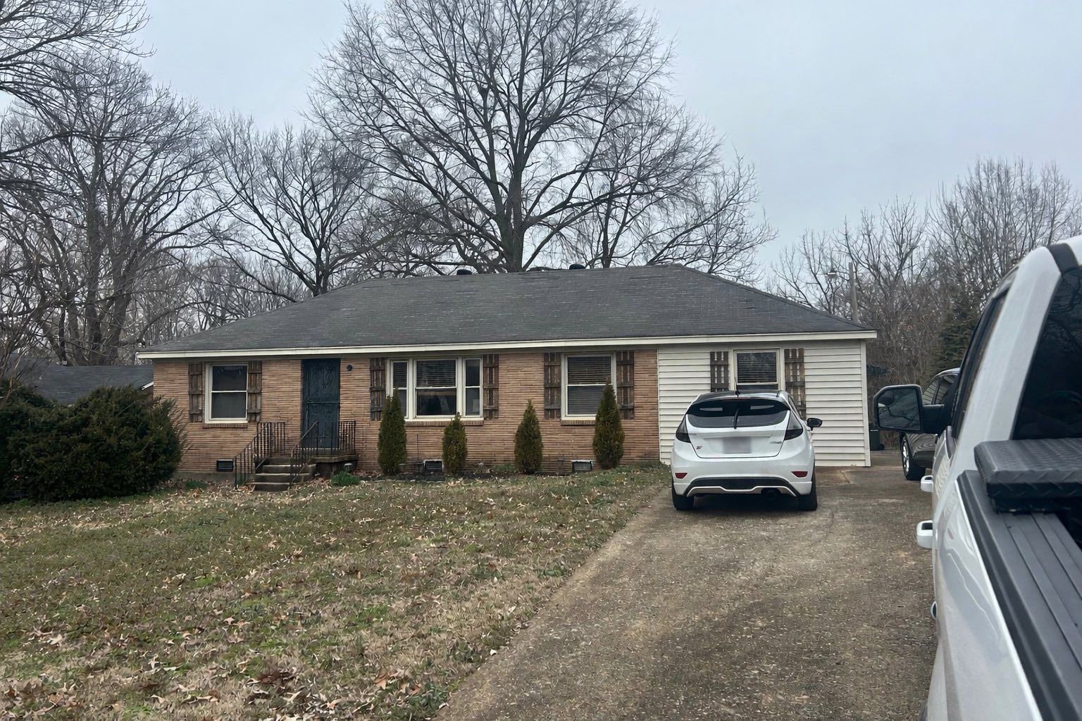 Single-story brick house with a driveway, white SUV, and bare trees in front yard.