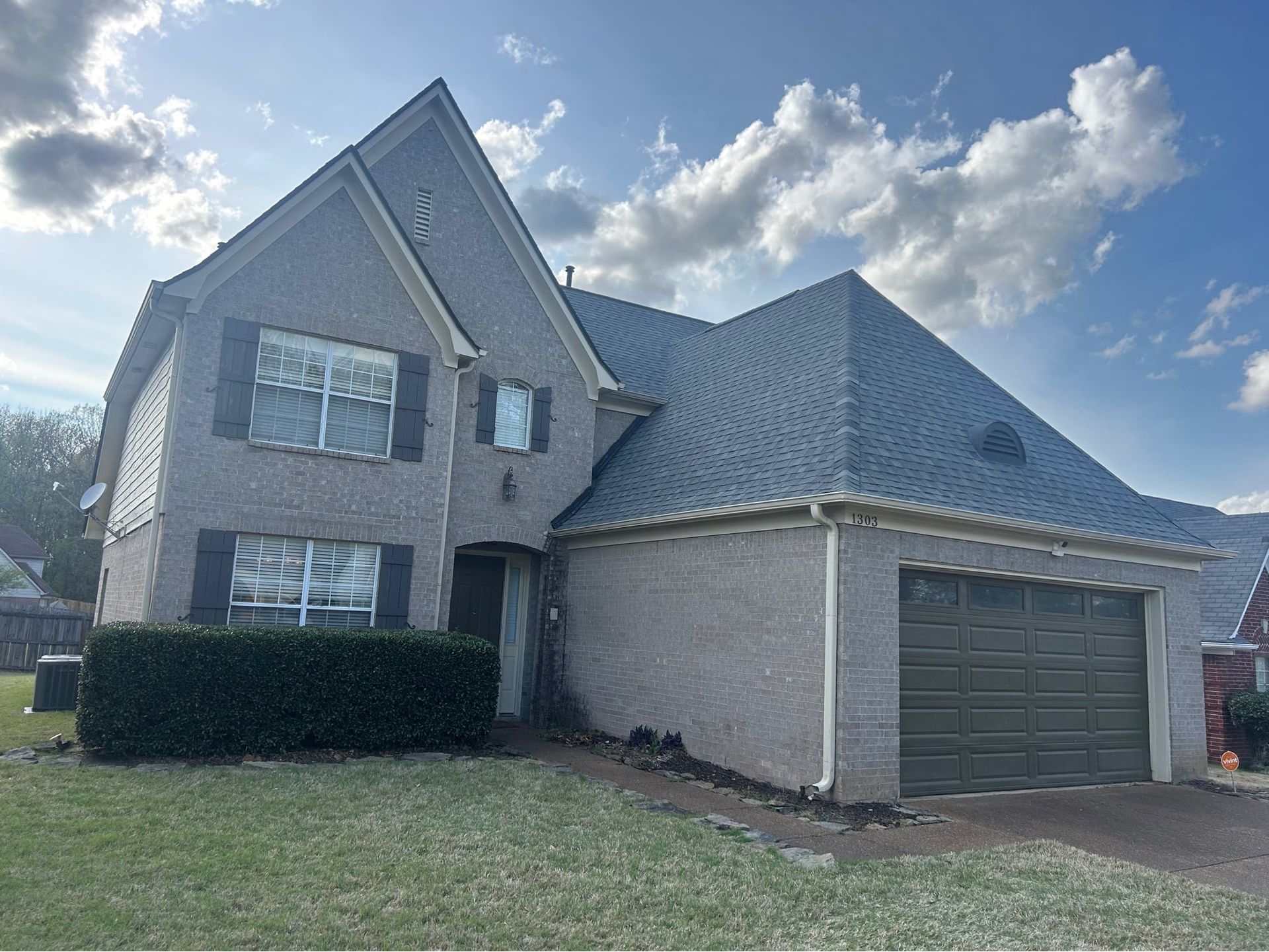 Two-story brick house with a dark gray roof, attached garage, and trimmed hedge on a grassy lawn.