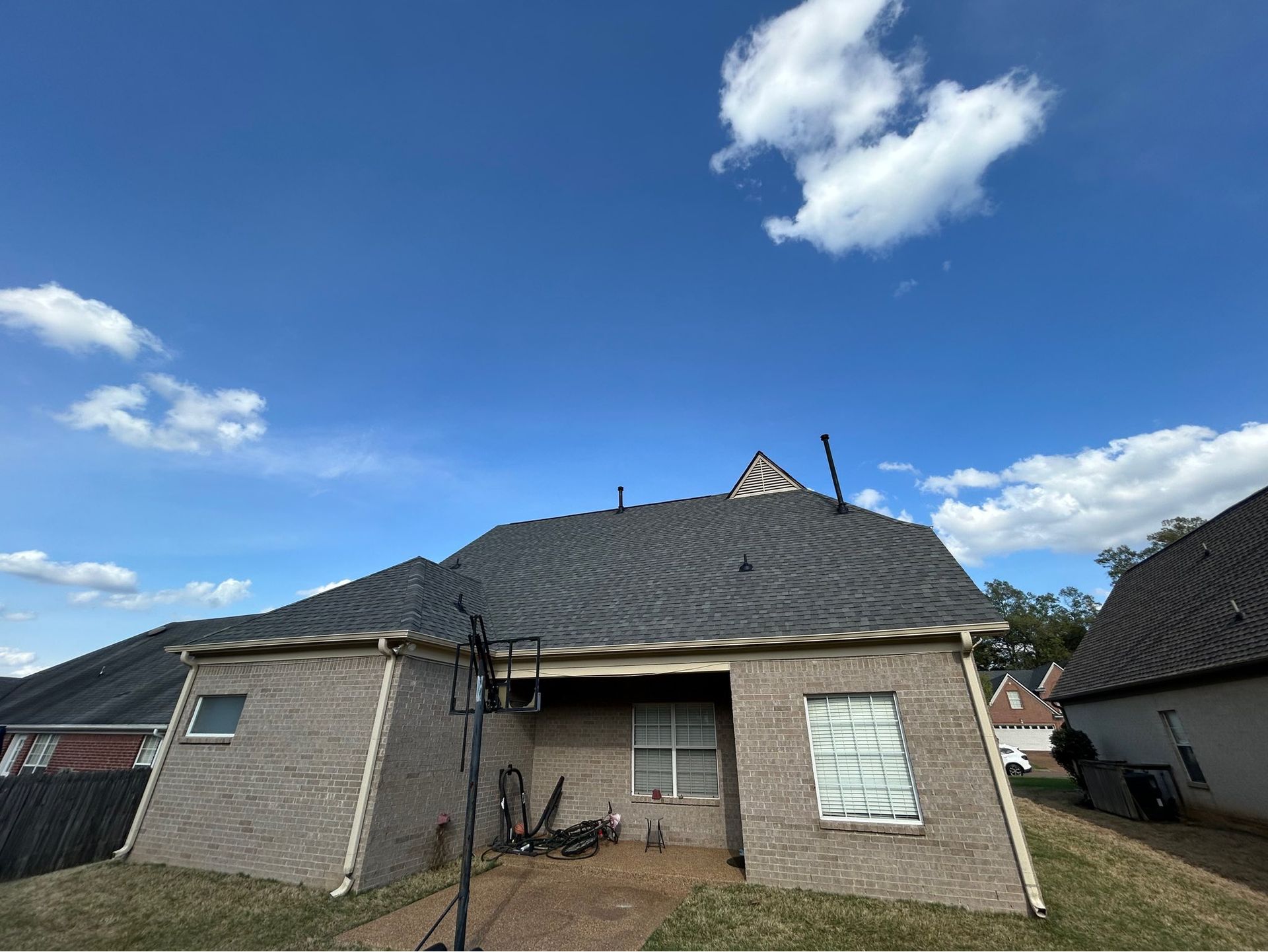 Small brick house with a dark roof and boarded windows under a bright blue sky.