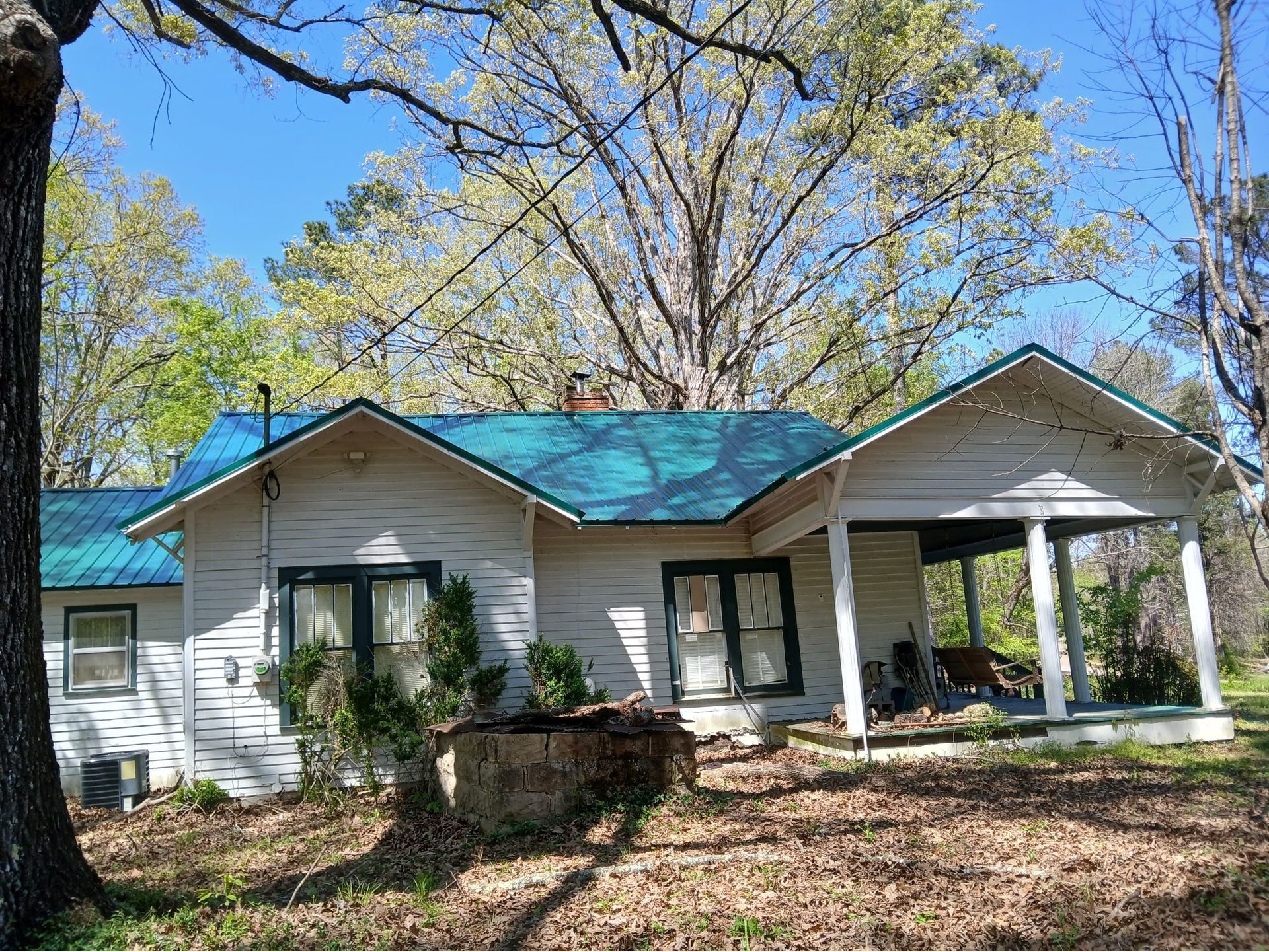 White house with teal roof and front porch surrounded by trees in a sunny yard