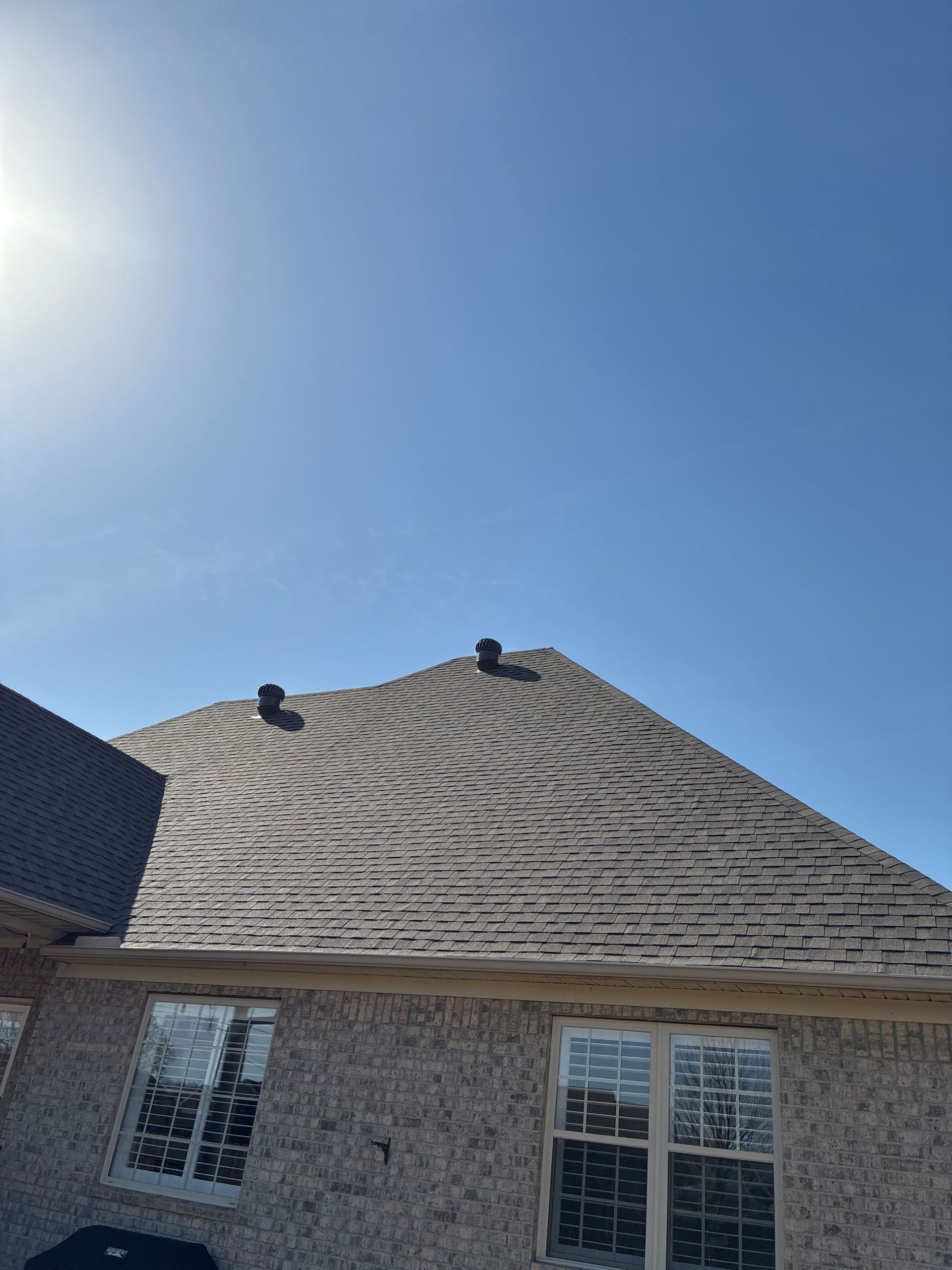 Suburban house roof under bright sun, with two roof vents and light stone exterior.