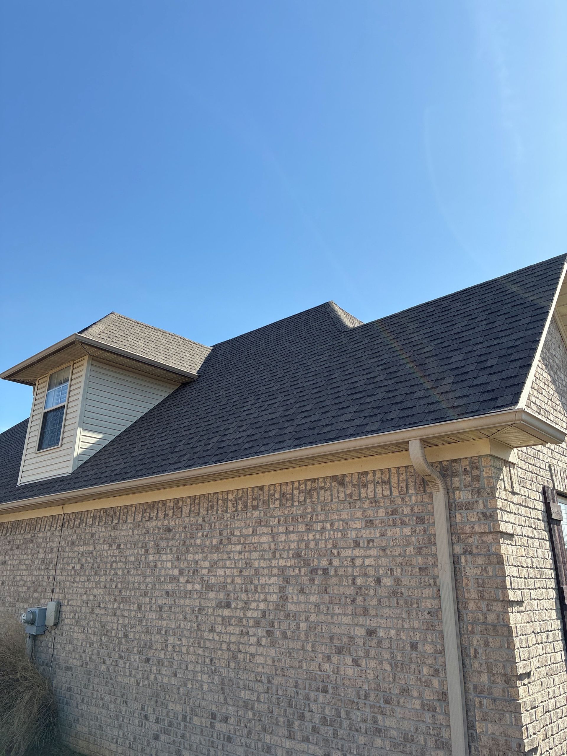 Suburban house with a dark shingle roof and stone exterior under a clear blue sky