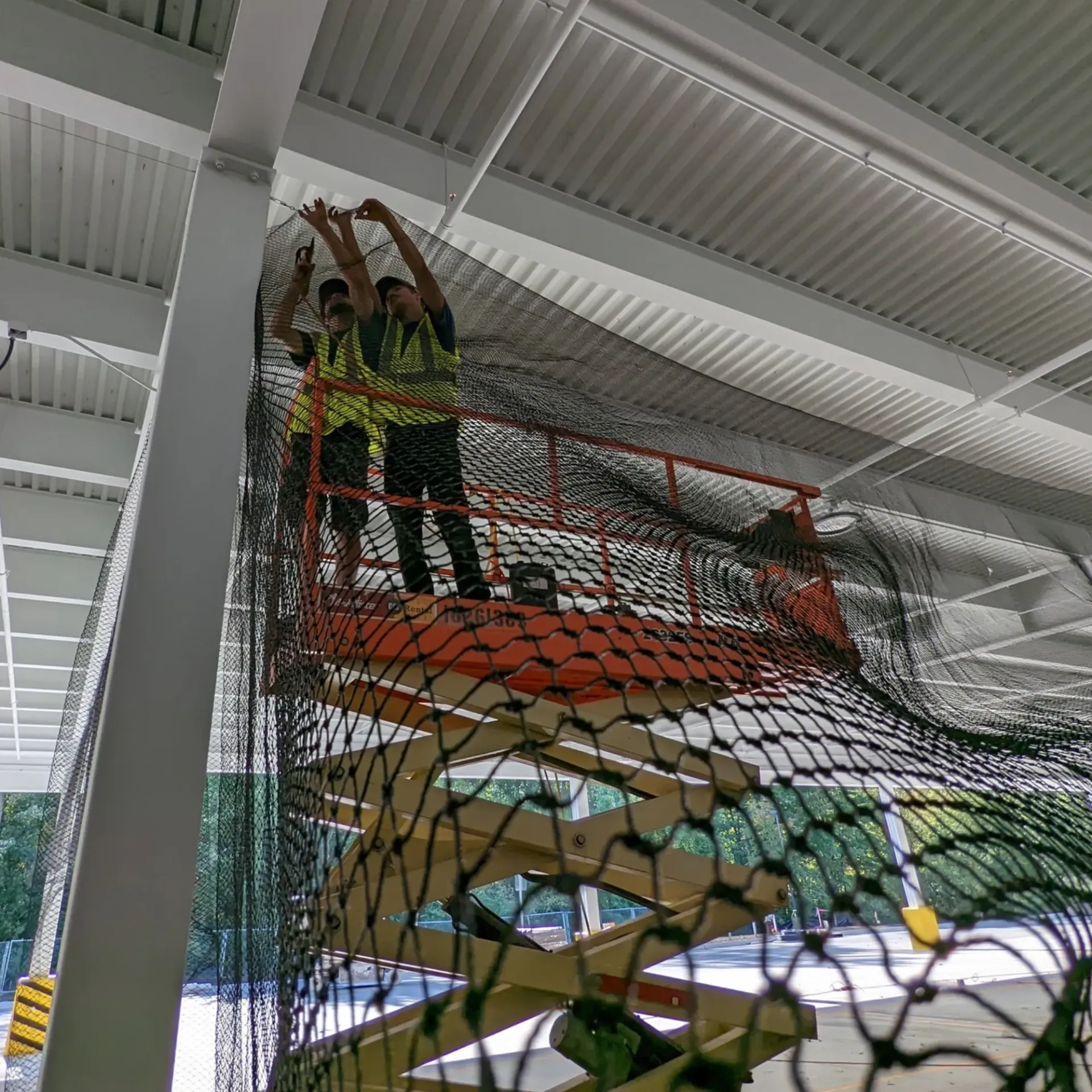 Michigan Wildlife Solutions - Two men are working on a safety net on a scissor lift.