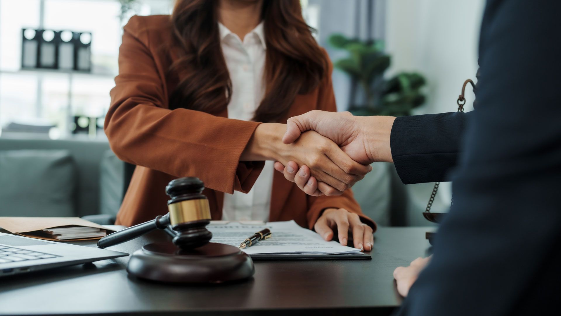 Lawyer shaking hands with a client over a desk with a gavel and documents.