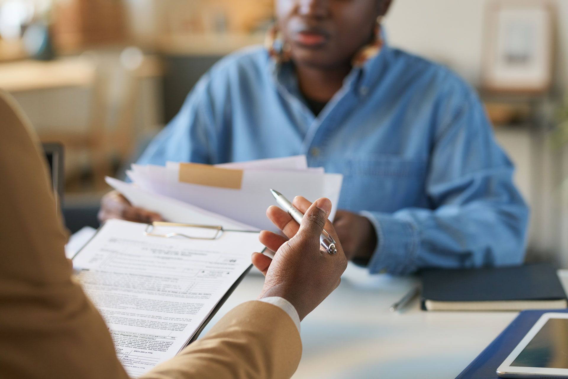 Person handing a pen over papers to another person at a table; they are reviewing documents.