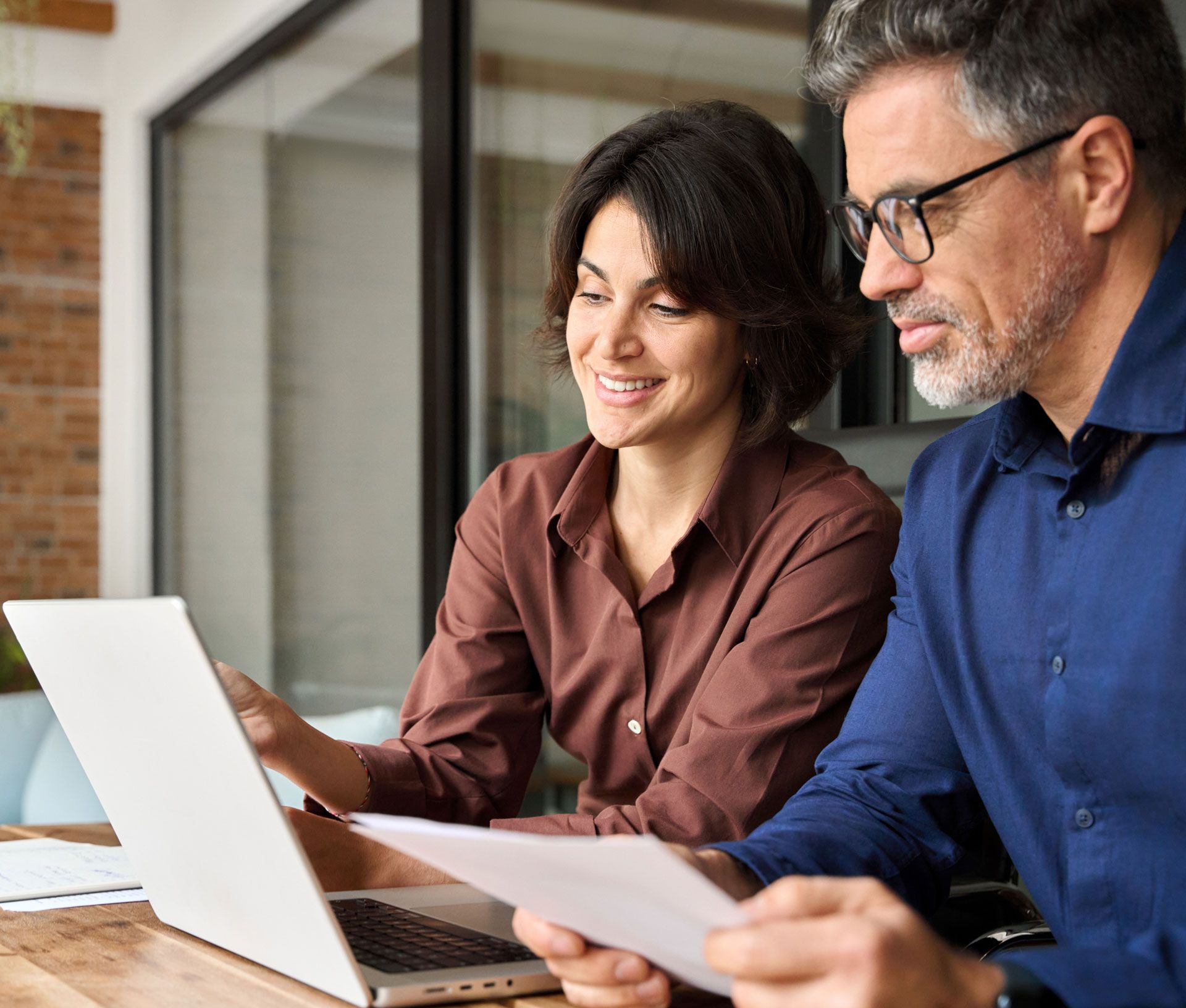 Woman and man looking at a laptop and documents, smiling in an office setting.