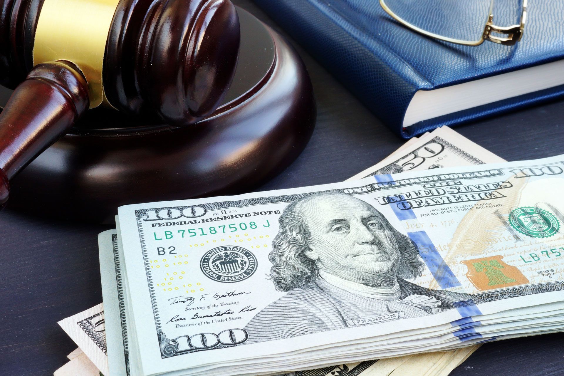 Gavel, stacks of $100 bills, and a law book, suggesting legal or financial proceedings.
