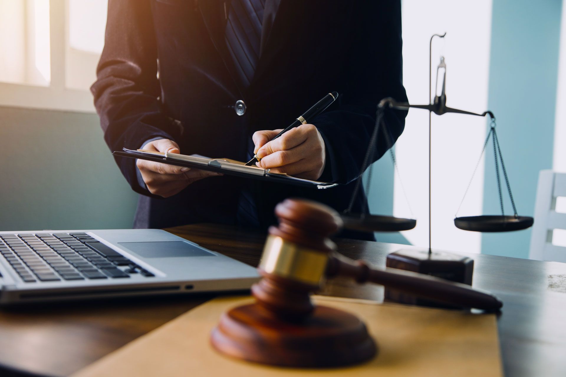 Gavel, scales of justice, laptop, and person in suit writing on a document.