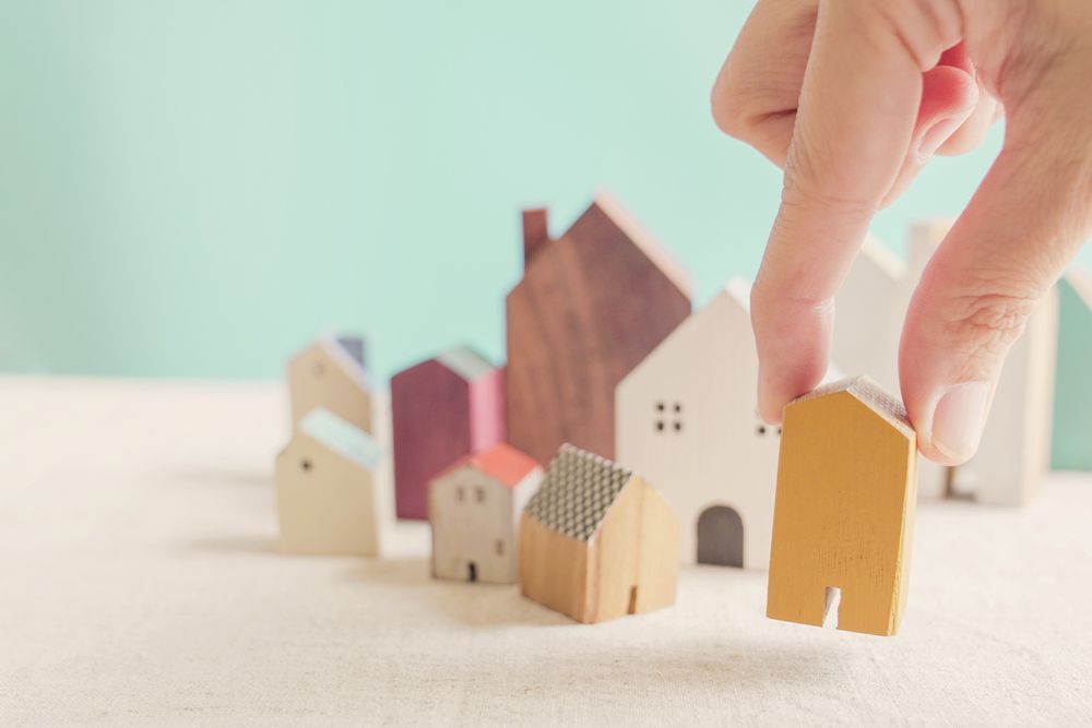 A Hand Places a Small Yellow Wooden House Model — Richardson Conveyancing In Terrigal, NSW