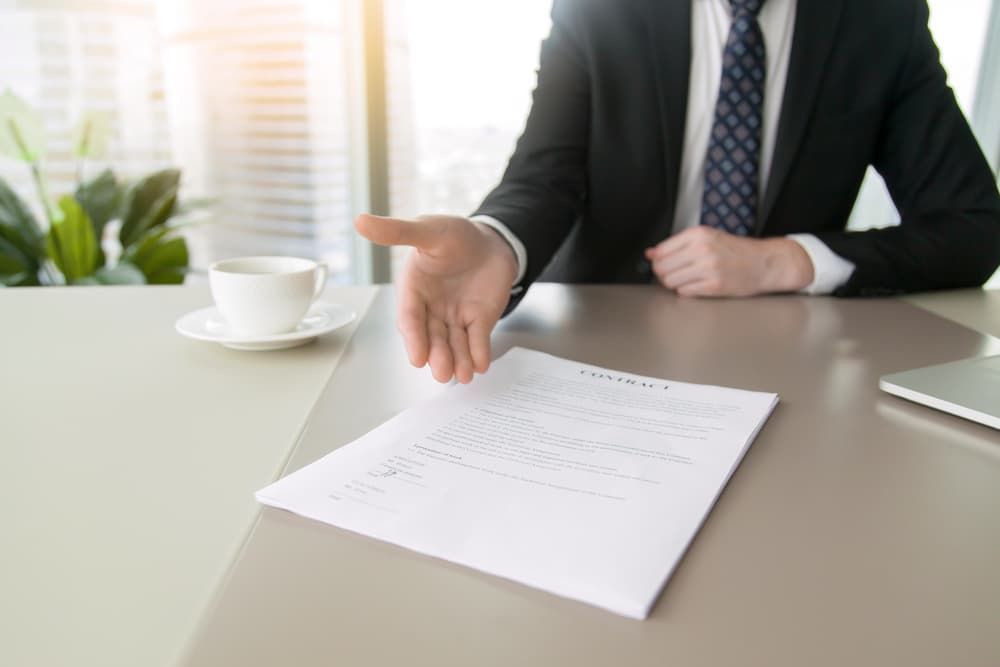 A Person in a Suit Gesturing Toward a Document on a Desk — Richardson Conveyancing In Tumbi Umbi, NSW