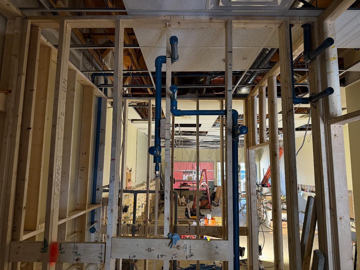 Construction site interior with exposed framing, scaffolding, and blue support poles in a narrow hallway.