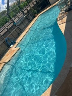 Blue swimming pool with rippling water beside a tan deck and black fence