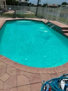 Backyard swimming pool with turquoise water, brick pavers, and a metal fence.