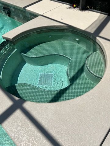 Round turquoise-tiled spa pool built into a concrete patio in bright sunlight.