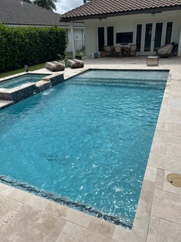 Backyard swimming pool with blue water, beige stone deck, and lounge chairs beside a house