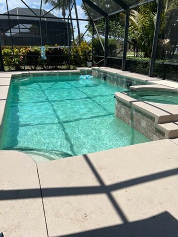 Covered backyard pool with turquoise water, screened enclosure, and tan stone deck in bright sunlight