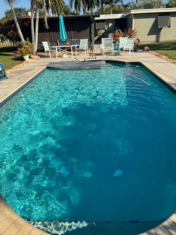 Backyard swimming pool with turquoise water, lounge chairs, and a patio with umbrellas.