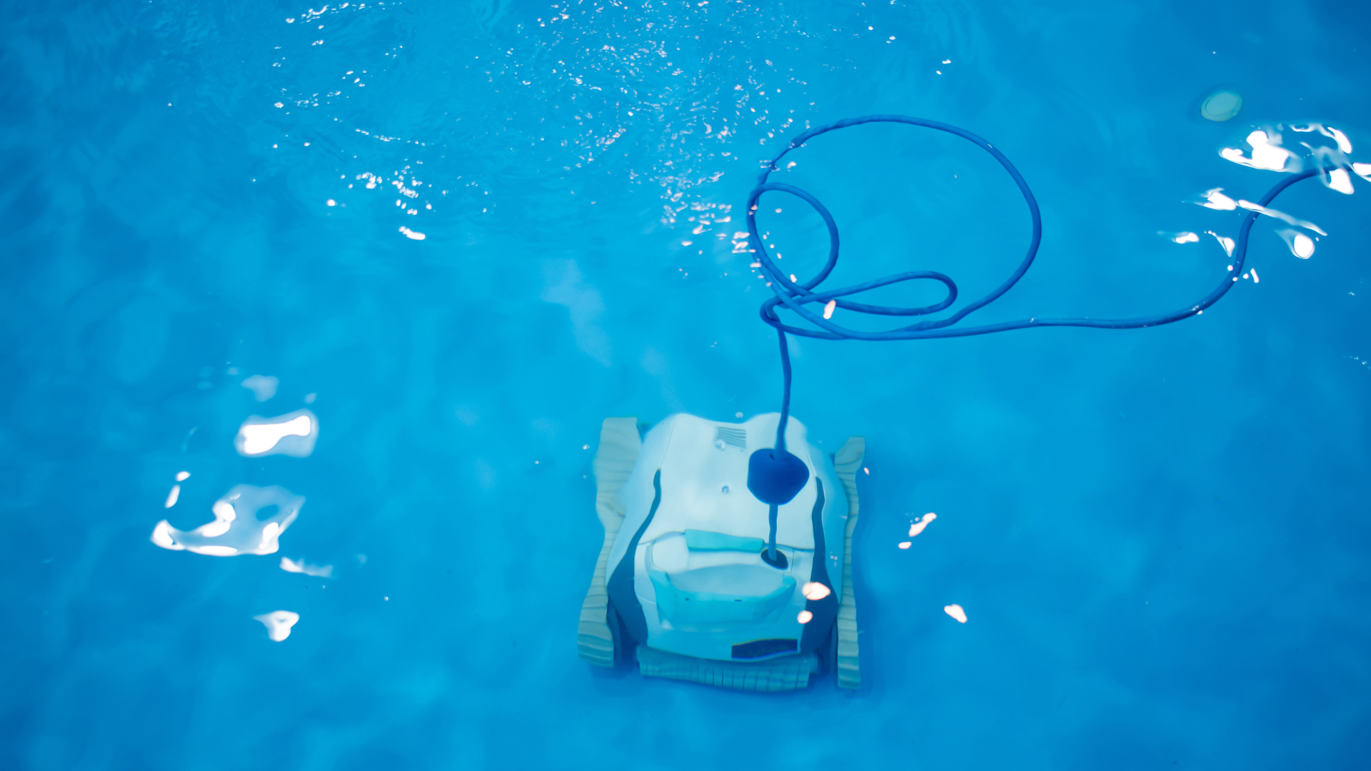 Robotic pool cleaner floating in blue water with a coiled cable visible