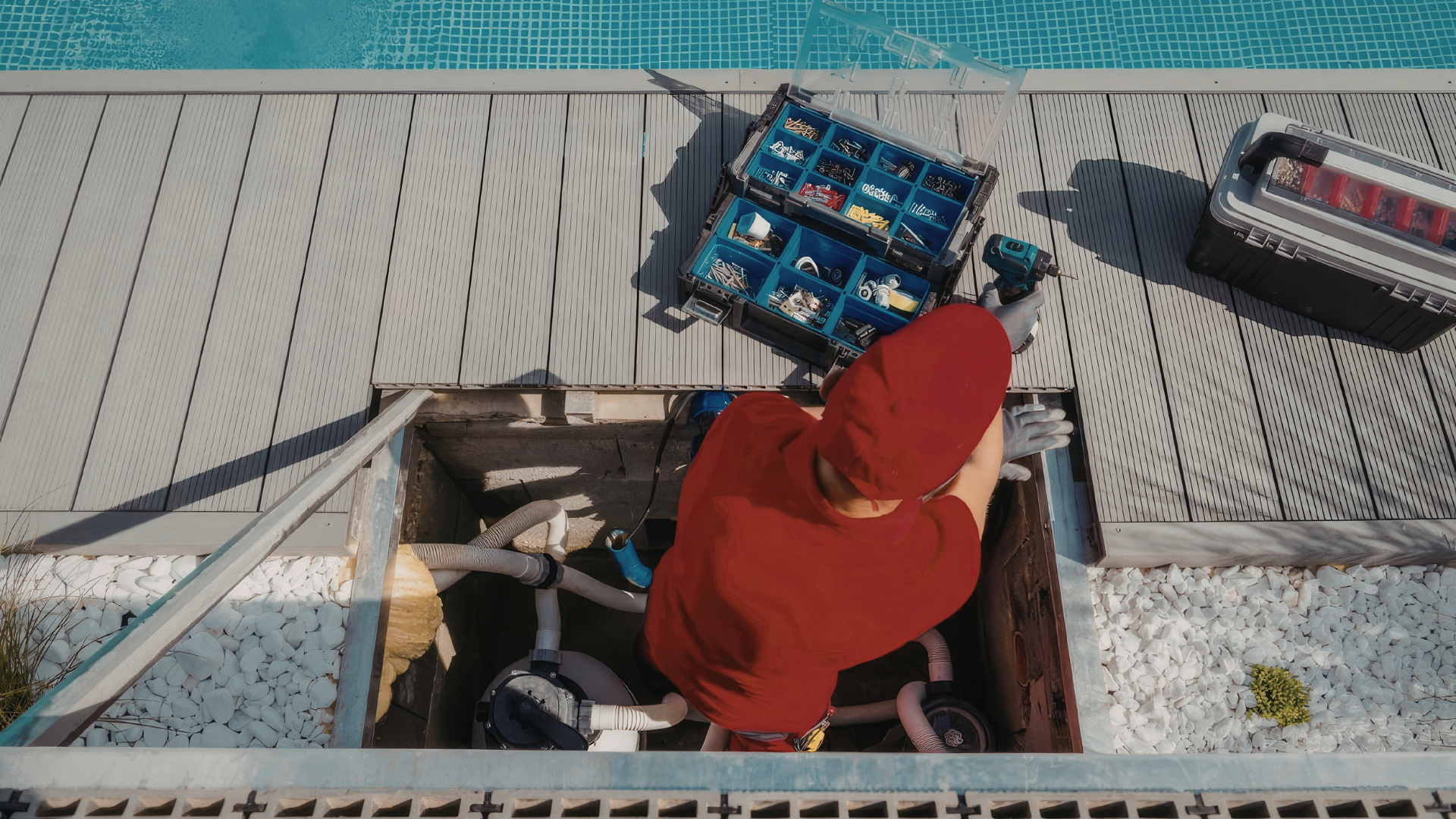 Person in a red hoodie working beside an open rooftop hatch with crates and equipment nearby.