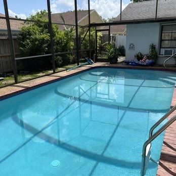Sunny backyard swimming pool with screened enclosure and patio seating