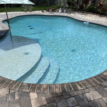 Curved backyard swimming pool with blue water, stone pavers, and steps at the edge.