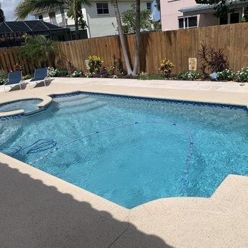 Backyard swimming pool with blue water, tan deck, lounge chairs, and a wooden fence.