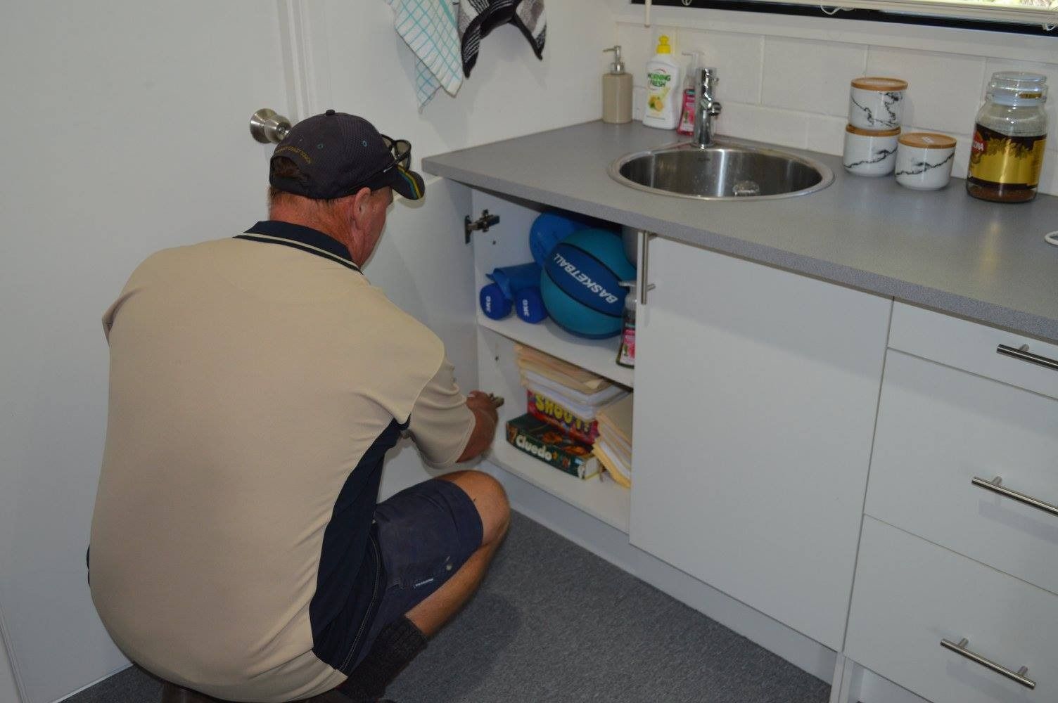 A Man Is Kneeling Down In Front Of A Sink In A Kitchen — Suncoast Termite & Pest In Nambour, QLD