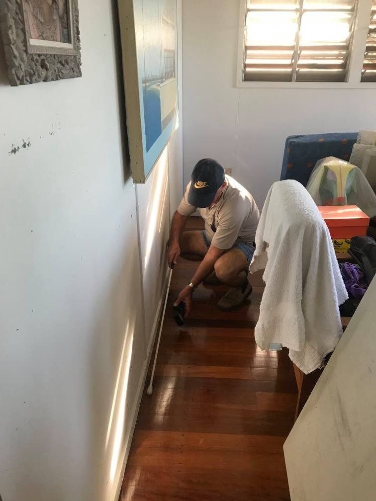 A Man Is Measuring A Wall In A Living Room — Suncoast Termite & Pest In Nambour, QLD
