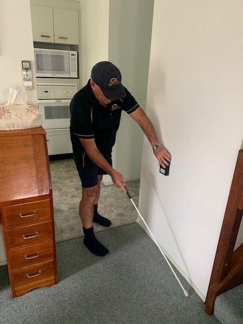 A Man Is Measuring A Wall With A Tape Measure — Suncoast Termite & Pest In Nambour, QLD