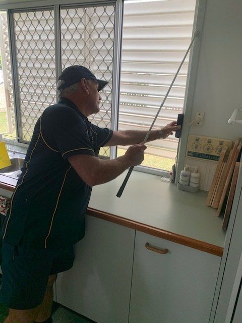 A Man Is Cleaning A Window With A Mop In A Kitchen — Suncoast Termite & Pest In Nambour, QLD