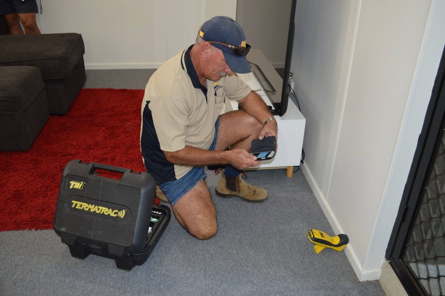 A Man Is Kneeling Down In Front Of A Television In A Living Room — Suncoast Termite & Pest In Nambour, QLD