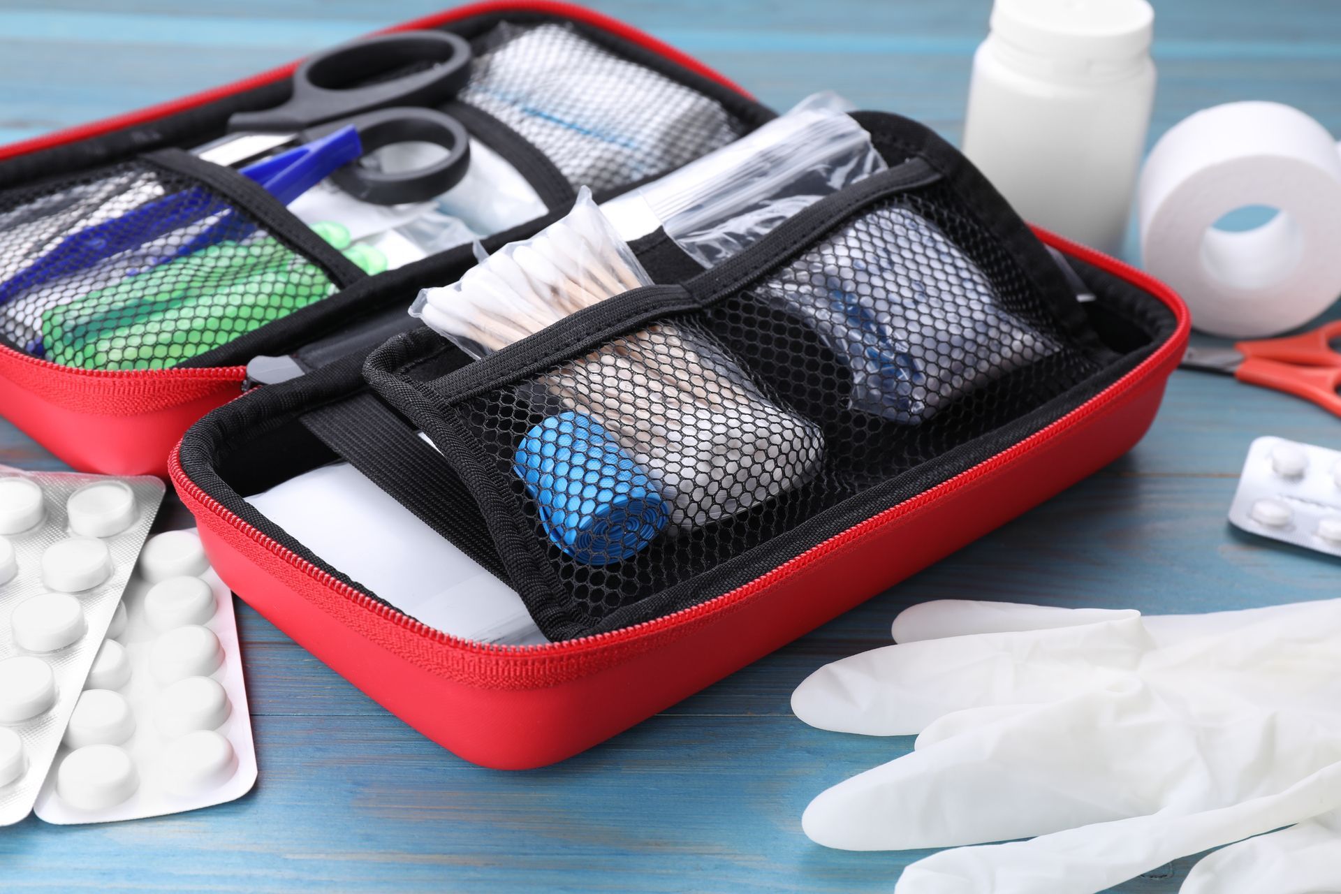 First-aid kit with supplies: bandages, gauze, medication, gloves, and scissors on a blue surface.