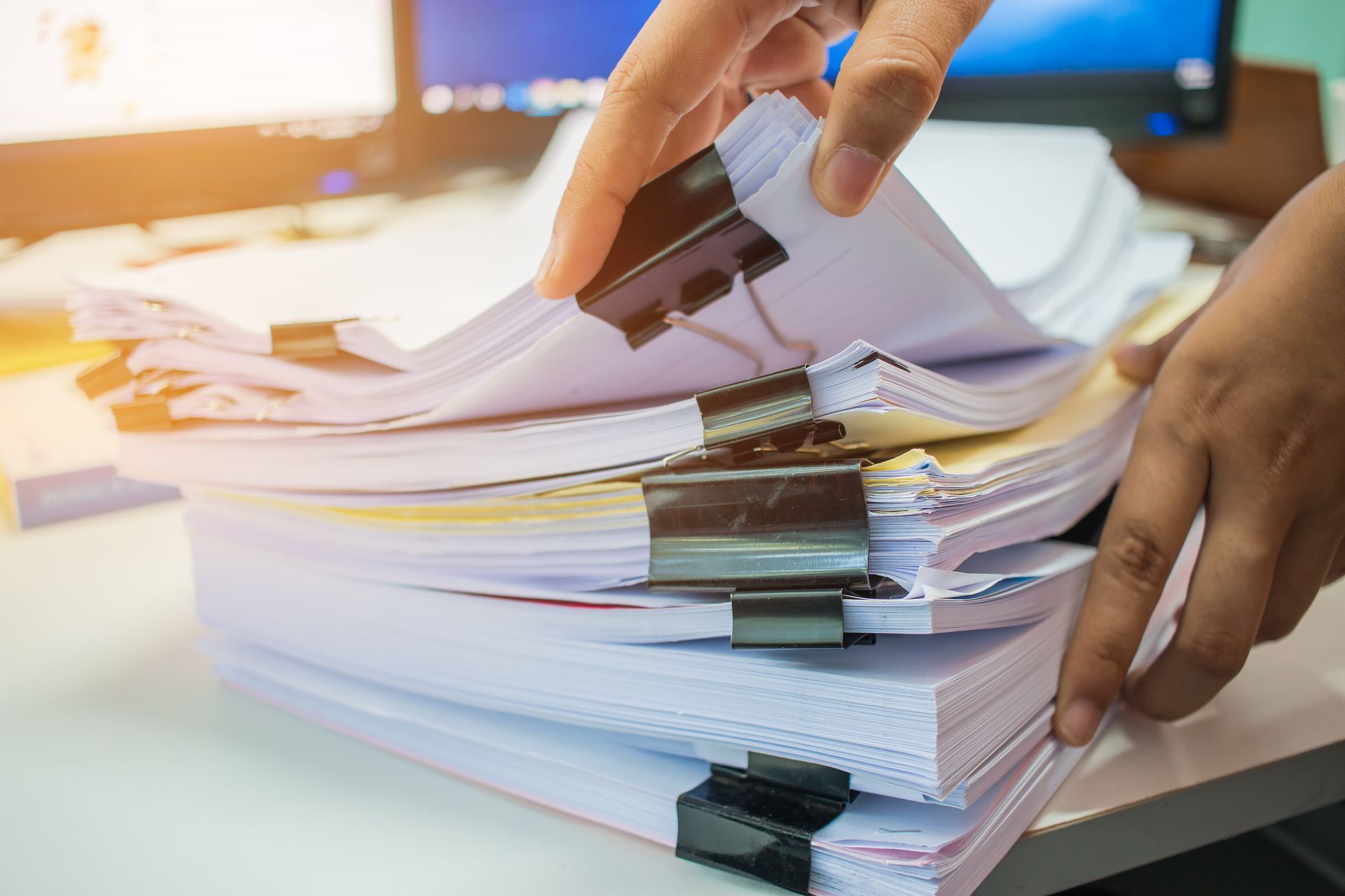 Hands holding stack of paperwork with black binder clips on white desk.