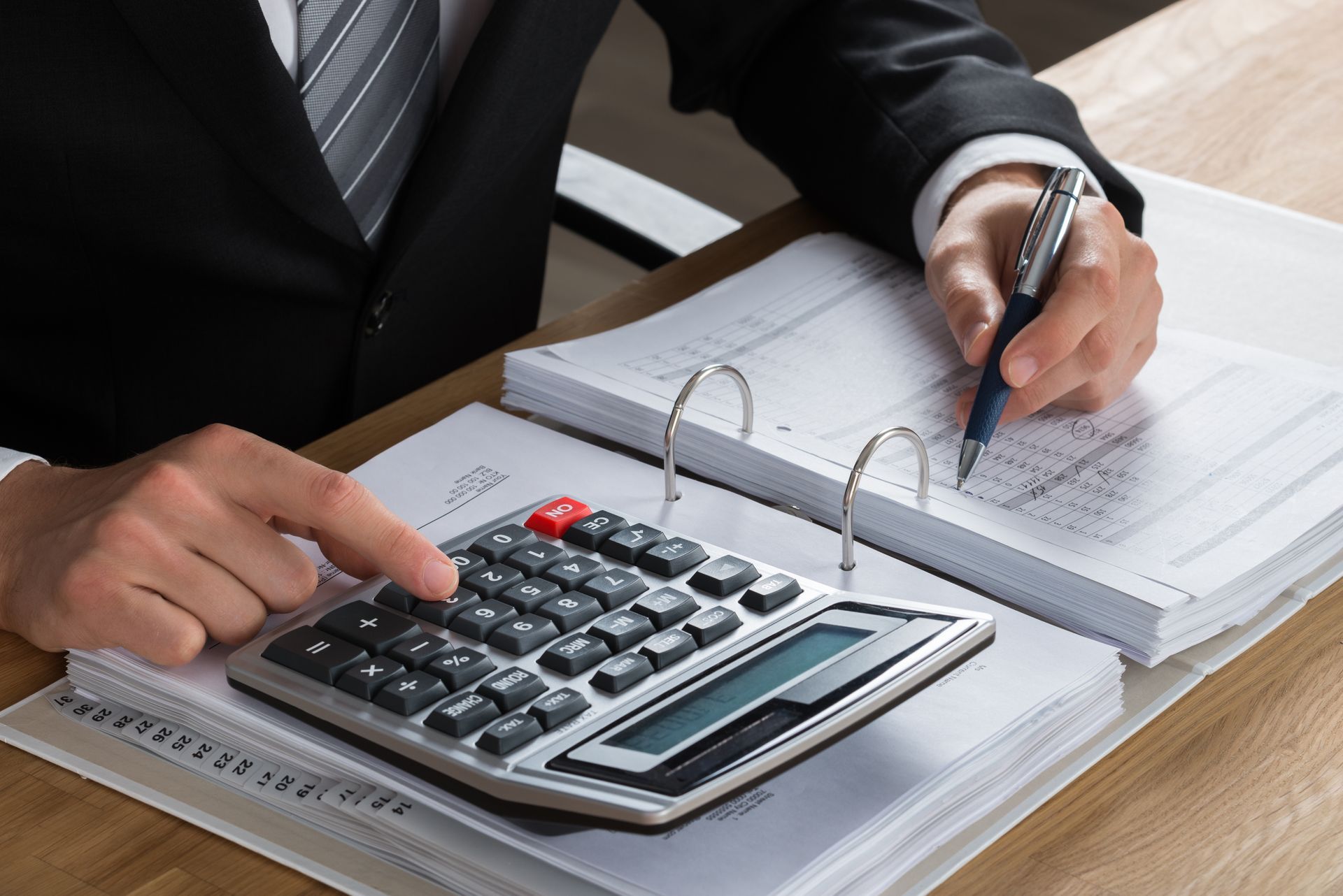 Person in suit uses calculator and pen on financial documents.