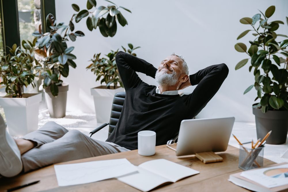 An older man in a chair with his feet up relaxes at his desk.