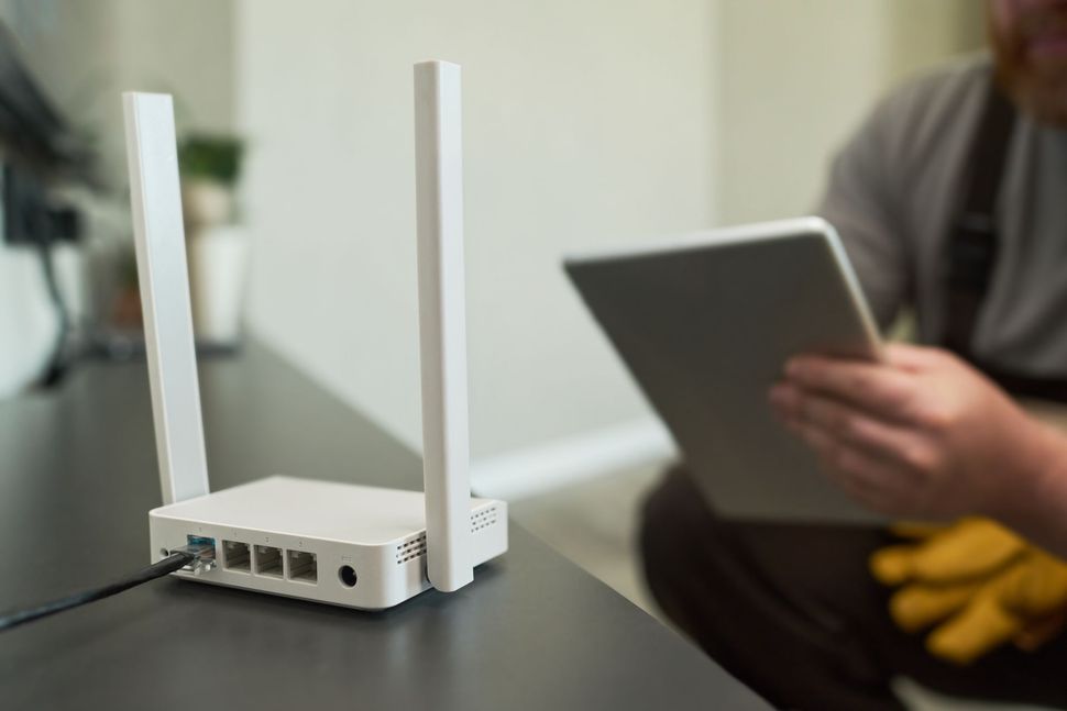 White Wi-Fi router with antennas on a table, a person holding a tablet is in the background. White Wi-Fi router with antennas on a table, a person holding a tablet is in the background.