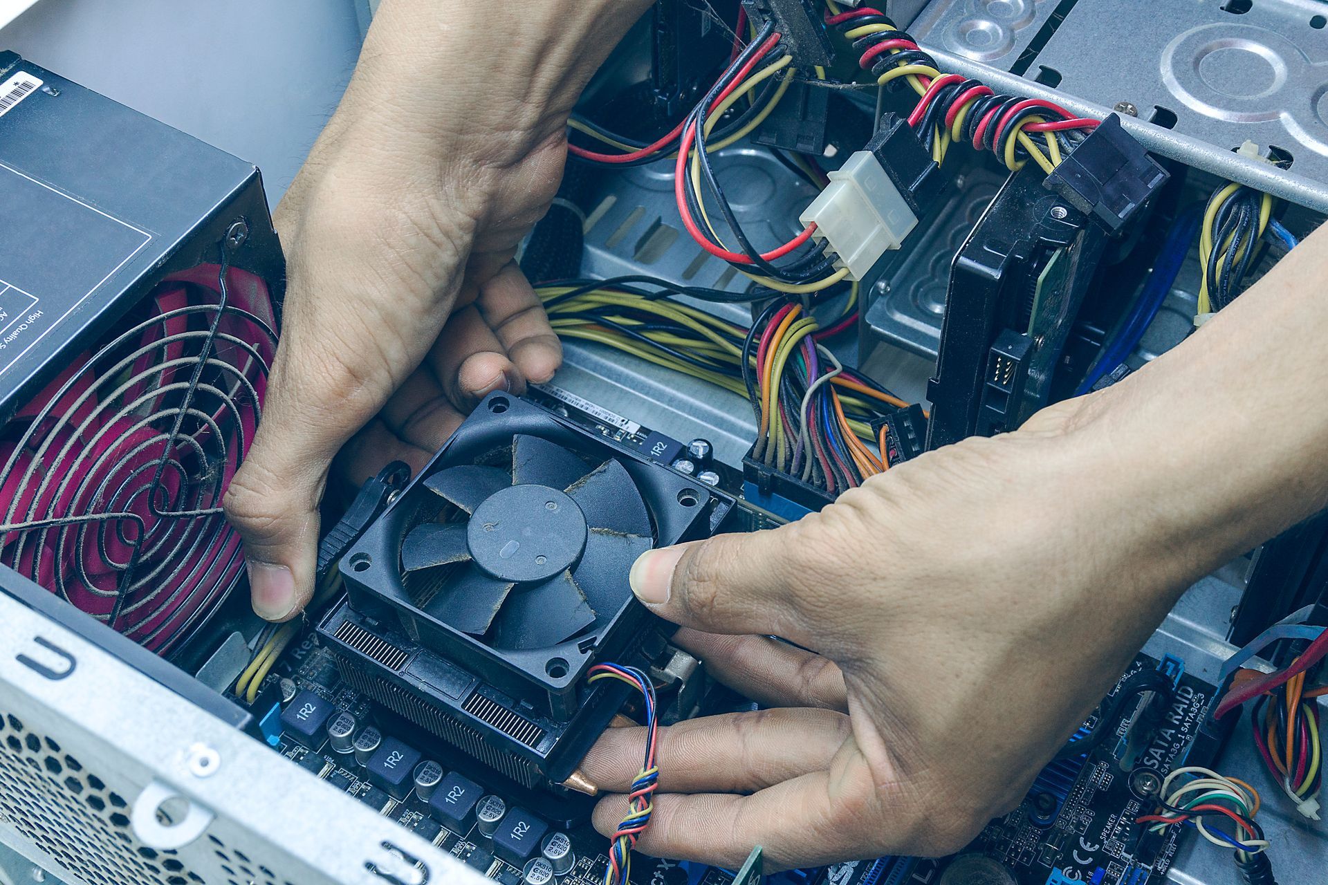 Hands installing a black CPU fan inside a computer case with colorful wires.