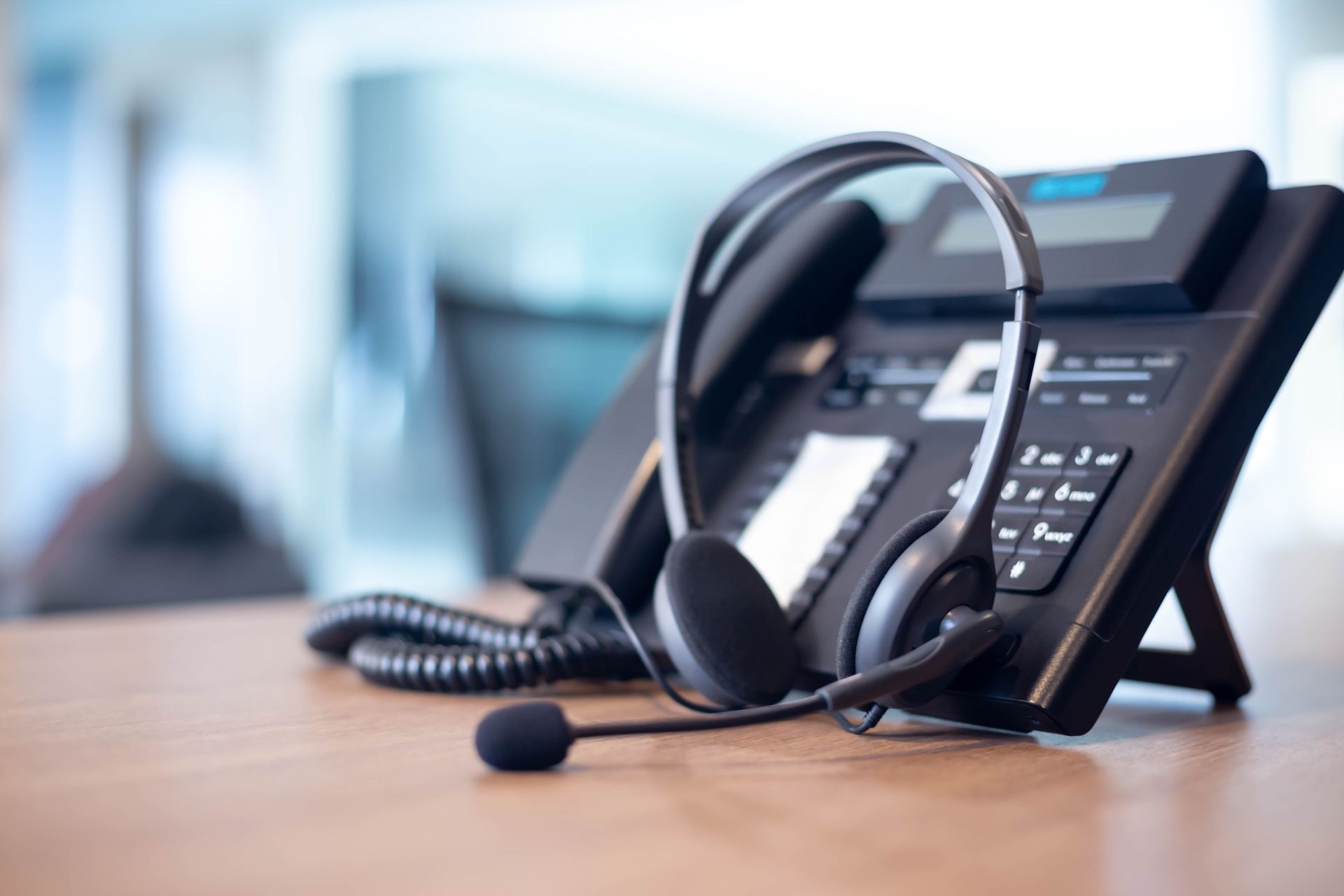 Headset resting on a black office phone, on a desk, in a blurred office setting.